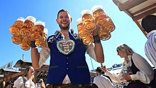 A waiter carries mugs of beer into the Hacker tent on the first day of Oktoberfest on Munich's Theresienwiese, Germany, Saturday, Sept. 20, 2025.