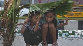Unas niñas se refugian bajo hojas de palmera durante un aguacero monzónico en Bombay, India, el domingo 21 de junio de 2026.