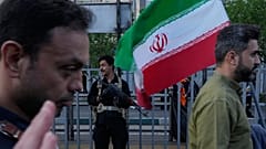 ARCHIVO: Un agente de seguridad monta guardia mientras un hombre porta una bandera iraní durante una marcha oficial en Teherán, 29 de abril de 2026
