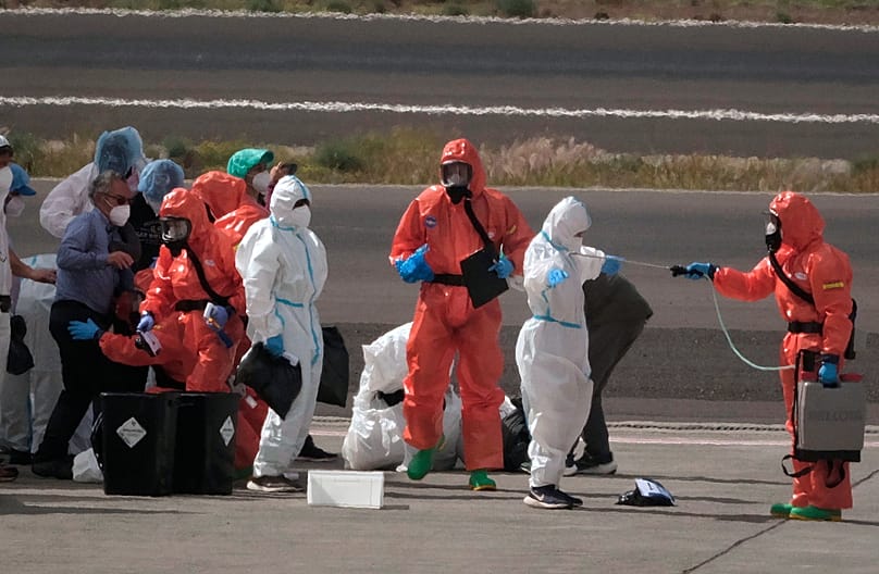 مسؤولون في الحكومة الإسبانية يرشون الركاب بمطهر قبل صعودهم إلى الطائرة، بعد نزولهم من السفينة السياحية 