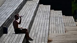 Ein Mann sitzt am Dienstag, dem 23. Juni 2026, im Park am Gleisdreieck in Berlin in der Sonne und trinkt Wasser.