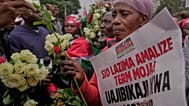 A relative of a person killed during the 2024 anti-government protests holds a sign with writing in Kiswahili reading "It's not a must to finish one term" 