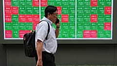 A man walks past a monitor showing stock prices of companies on the Tokyo Stock Exchange, 23 June 2026