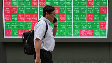 A man walks past a monitor showing stock prices of companies on the Tokyo Stock Exchange, 23 June 2026