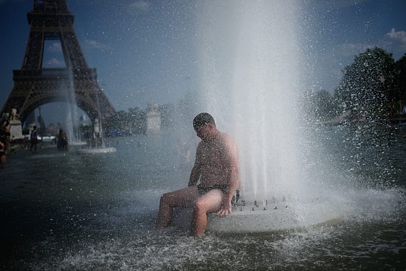 شخص يبرد نفسه عند نافورة تروكاديرو بالقرب من برج إيفل أثناء موجة الحر في باريس، الأربعاء 24 يونيو 2026. (AP Photo/كريستوف إينا)