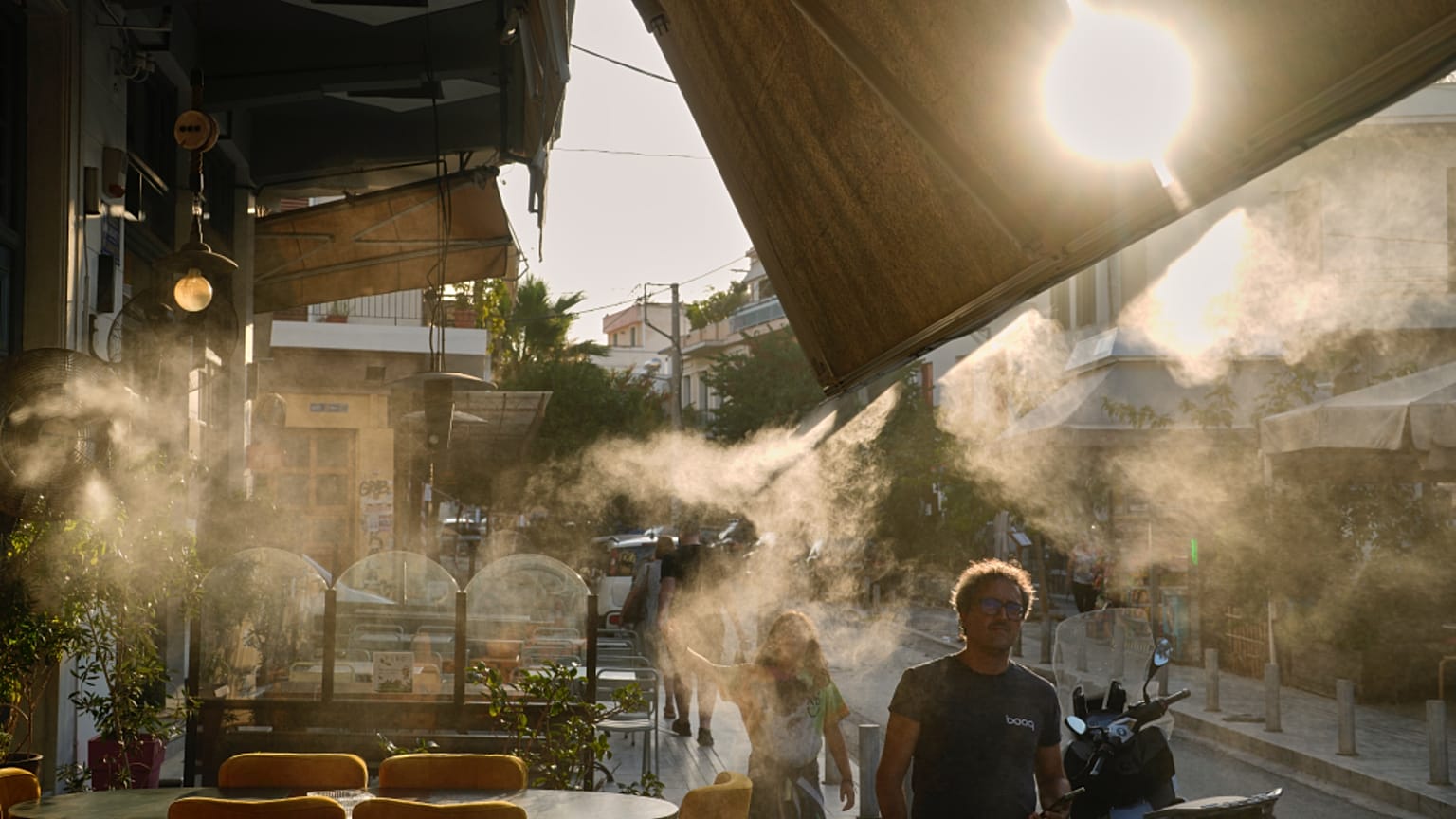 Peões passam junto de um aparelho de nebulização no bairro de Thissio, em Atenas, durante uma vaga de calor em julho de 2025.