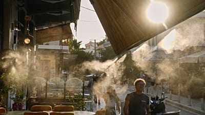 Peões passam junto de um aparelho de nebulização no bairro de Thissio, em Atenas, durante uma vaga de calor em julho de 2025.