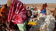 لاجئ سوداني يحمل طفلاً أثناء انتظاره لجمع إمدادات المياه في مخيم أبو شوك للاجئين خارج بلدة الفاشر بدارفور بالسودان