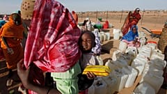 لاجئ سوداني يحمل طفلاً أثناء انتظاره لجمع إمدادات المياه في مخيم أبو شوك للاجئين خارج بلدة الفاشر بدارفور بالسودان