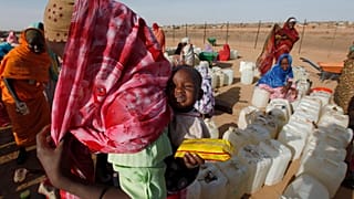 لاجئ سوداني يحمل طفلاً أثناء انتظاره لجمع إمدادات المياه في مخيم أبو شوك للاجئين خارج بلدة الفاشر بدارفور بالسودان