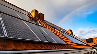 Solar panels on a roof, with a rainbow in the distance. 