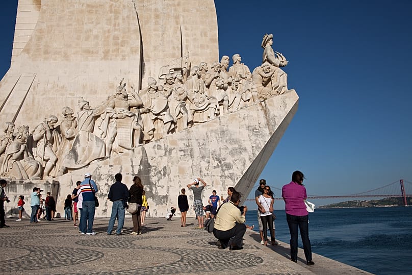 Tourists take pictures by the Padrão dos Descobrimentos, or Monument to the Discoveries, on the bank of the Tagus river in Lisbon, Portugal.