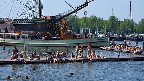 Persone si rinfrescano vicino alla replica di una nave VOC del XVIII secolo durante un'ondata di caldo ad Amsterdam, Paesi Bassi, 25 giugno 2026.