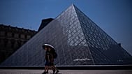 Tourists with an umbrella walk near the Louvre museum during a heat wave in Paris, Saturday, June 27, 2026.