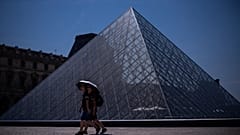 Tourists with an umbrella walk near the Louvre museum during a heat wave in Paris, Saturday, June 27, 2026.