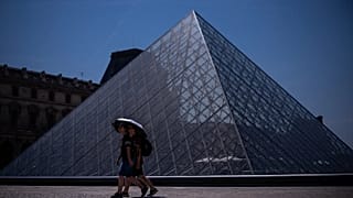 Tourists with an umbrella walk near the Louvre museum during a heat wave in Paris, Saturday, June 27, 2026.