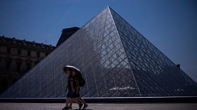 Tourists with an umbrella walk near the Louvre museum during a heat wave in Paris, Saturday, June 27, 2026.