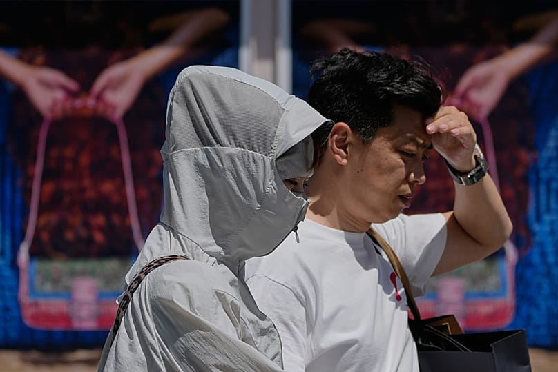 Una donna con abiti protettivi contro il sole attraversa in una giornata torrida un centro commerciale all'aperto a Pechino. Foto di lunedì 1º giugno 2026.
