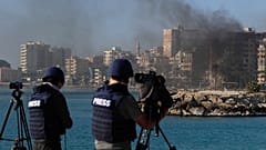 صحفيون يمارسون عملهم بينما يتصاعد الدخان من مبنى أصيب في غارة جوية إسرائيلية في مدينة صور بجنوب لبنان، يوم الاثنين 28 أكتوبر 2024.