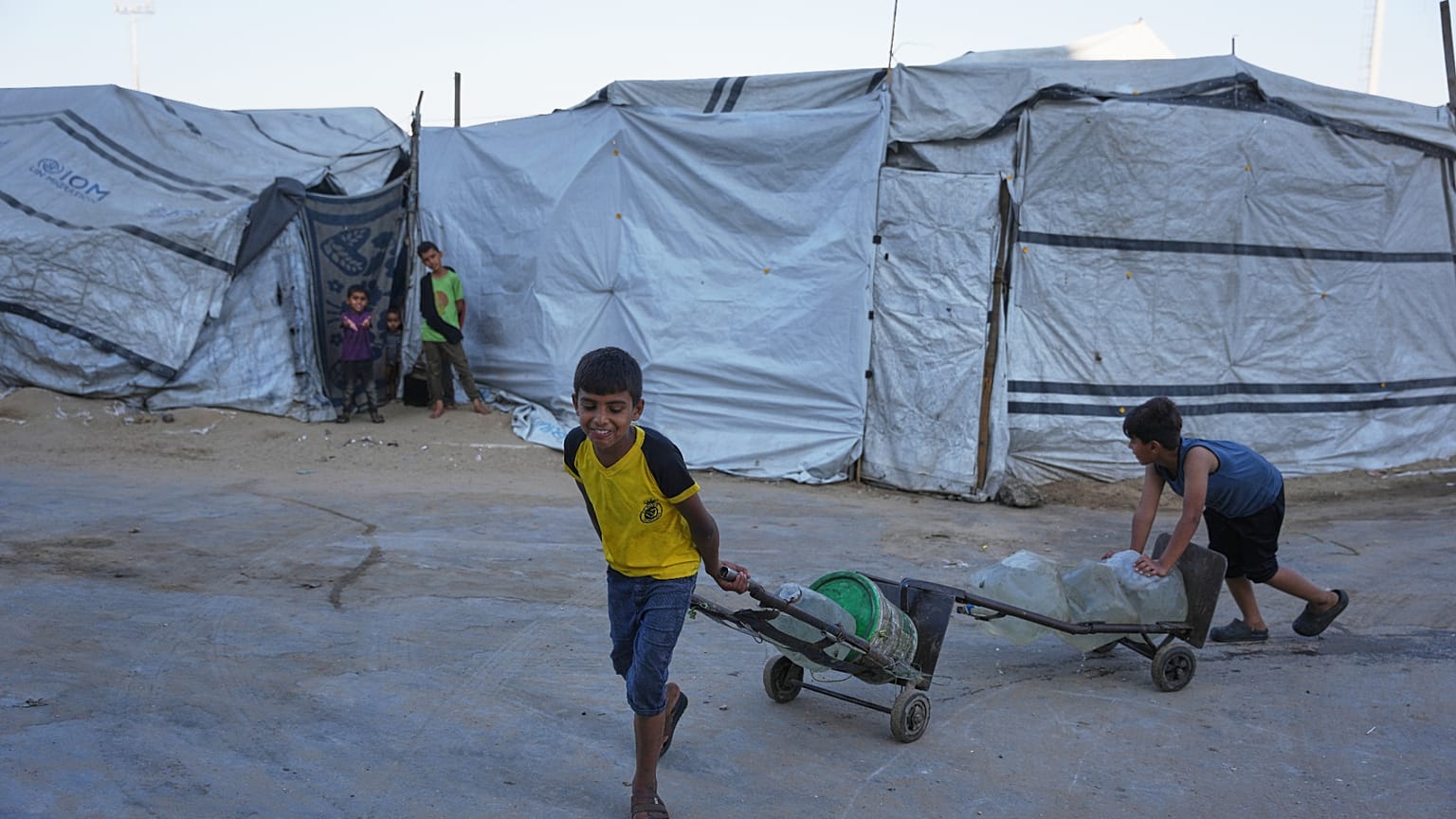 أطفال فلسطينيون نازحون ينقلون حاويات مياه في ملعب اليرموك المتضرر جراء الحرب الإسرائيلية على غزة، بمدينة غزة.