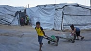 أطفال فلسطينيون نازحون ينقلون حاويات مياه في ملعب اليرموك المتضرر جراء الحرب الإسرائيلية على غزة، بمدينة غزة.