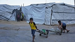 أطفال فلسطينيون نازحون ينقلون حاويات مياه في ملعب اليرموك المتضرر جراء الحرب الإسرائيلية على غزة، بمدينة غزة.