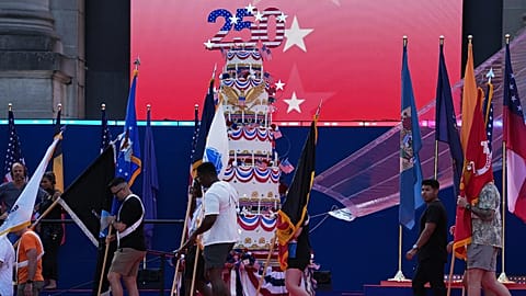 Az emberek zászlókat visznek egy óriási születésnapi torta mellett az America 250 brüsszeli rendezvényen.