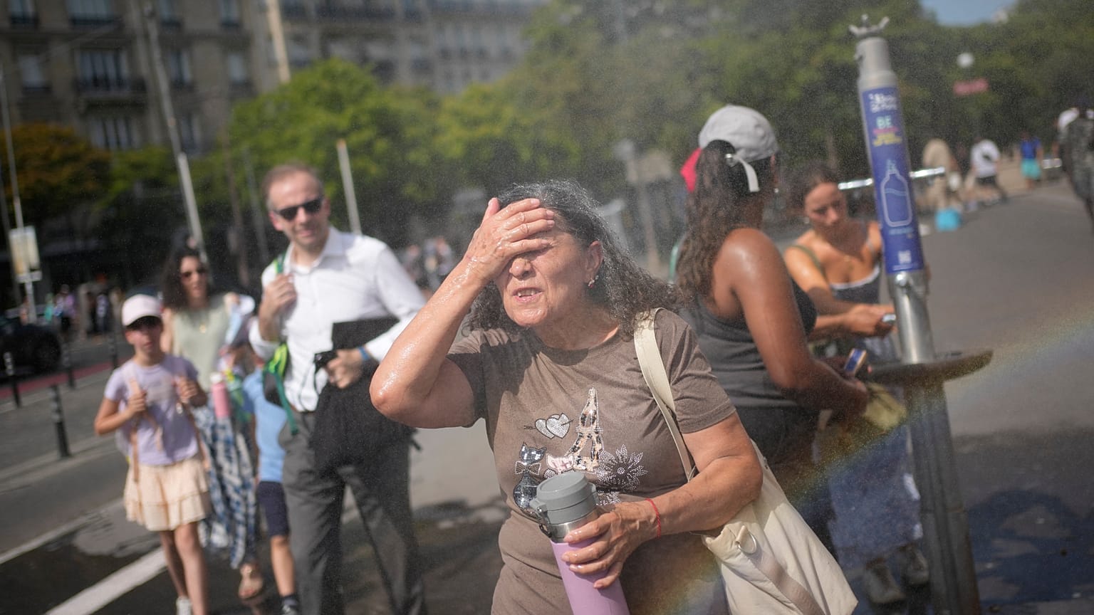 Tourists enjoy cooling off at a public water fountain In Paris, Friday, June 26, 2026. (AP Photo/Christophe Ena )