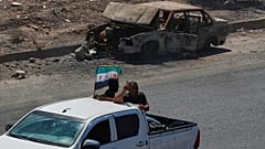  مقاتلون يستقلون الجزء الخلفي من شاحنة صغيرة ترفع العلم السوري، أثناء مرورهم بجوار سيارة محترقة على الطريق السريع الواصل بين درعا ودمشق في سوريا
