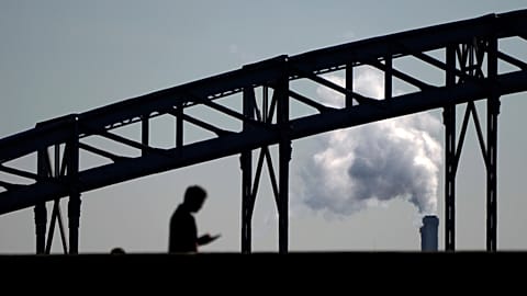 A man looks his phone while walking on a bridge with the smoke of a waste incinerator in background on the outskirts of Paris, Thursday, Sept. 23, 2021. 