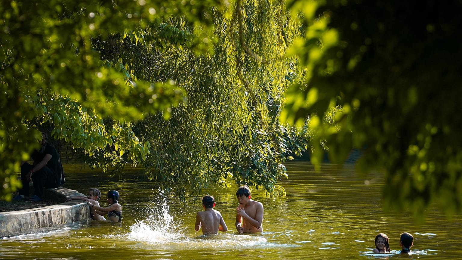 Dei ragazzi giocano in un lago in una giornata torrida, mentre il servizio meteo emette un'allerta rossa per il caldo estremo in gran parte del Paese, a Bucarest, Romania.