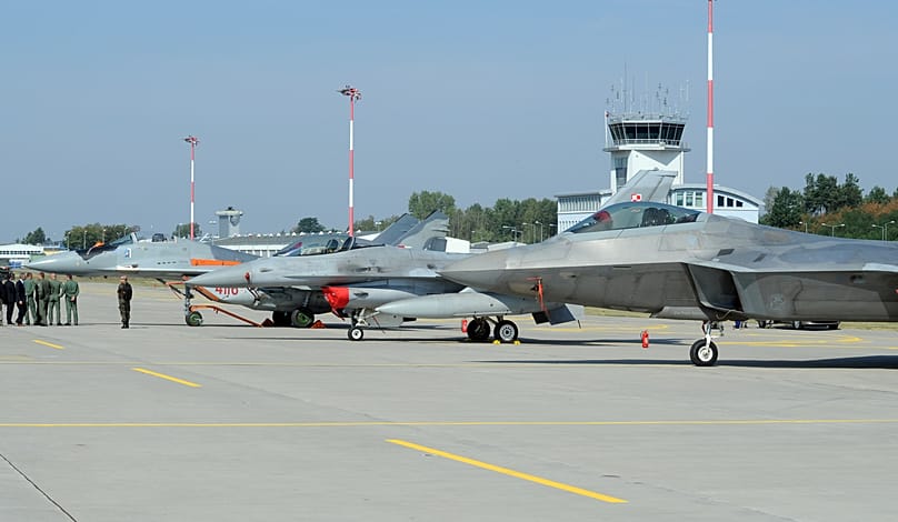 Officials walk past fighter jets parked on the apron, a Polish Air Force Mig-29, F-16, and F-22 Raptor at a military base in Lask, Poland, Aug. 31, 2015