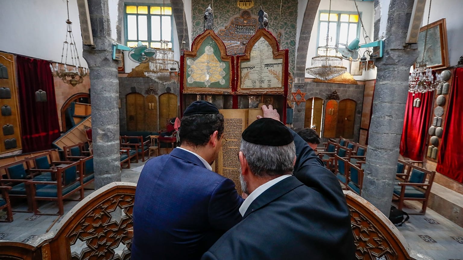 الحاخام يوسف حمرا، على اليمين، وابنه هنري يراقبان كتابًا مقدسًا قديمًا في كنيس إفرانج في مدينة دمشق القديمة في 18 فبراير 2025.