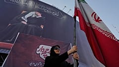 تحمل امرأة مؤيدة للحكومة العلم الإيراني تحت لافتة تحمل صورة المرشد الأعلى الراحل، علي خامنئي، في أحد ميادين وسط العاصمة طهران، إيران، الثلاثاء 30 يونيو/حزيران 2026.