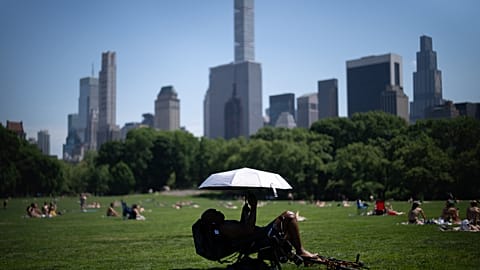 A person uses an umbrella to shield themselves from the sun during a heat advisory in Central Park