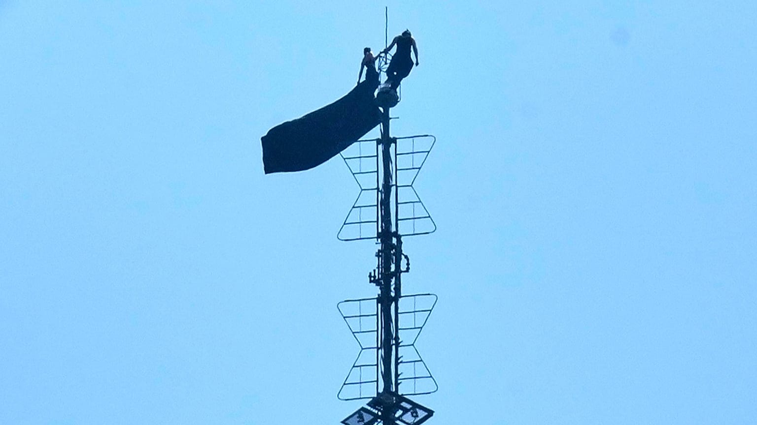 Two people stand on the tip of the antenna of the Empire State Building while holding a banner, 1 July, 2026
