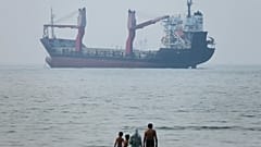 Un grupo de personas permanece en aguas poco profundas mientras un carguero aparece anclado en el estrecho de Ormuz, frente a Bandar Abbas, Irán, martes 30 de junio de 2026.