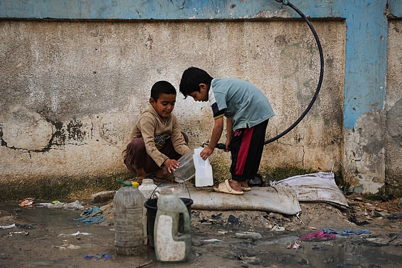 FILE - Palestinian children fill plastic bottles with water at a tent camp in Deir al-Balah, Gaza Strip, Thursday, Jan. 29, 2026. 