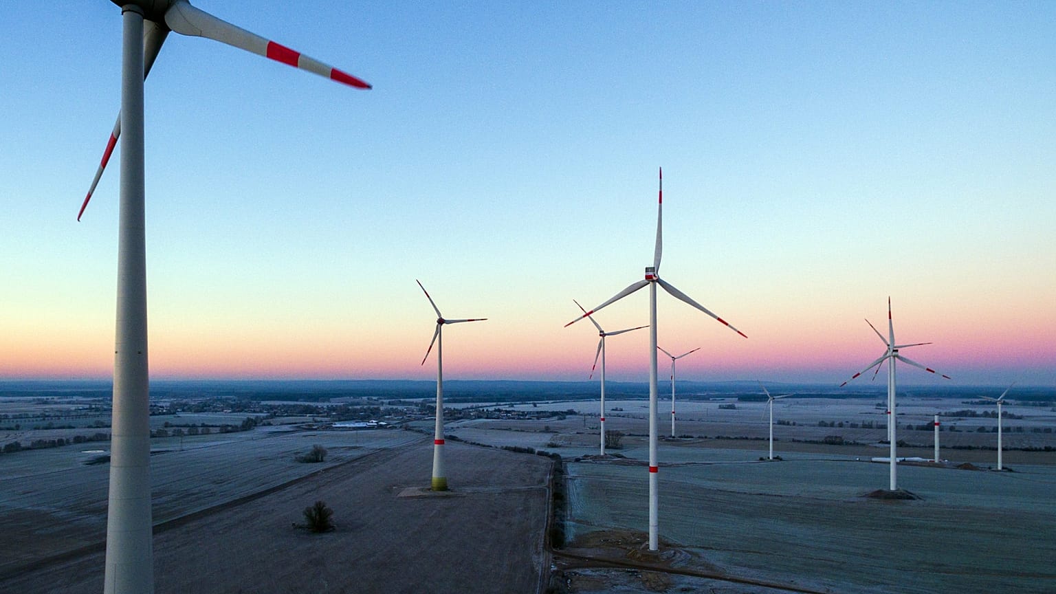 Sun rising in the morning sky above a landscape with a wind energy park near Jacobsdorf, Germany. 