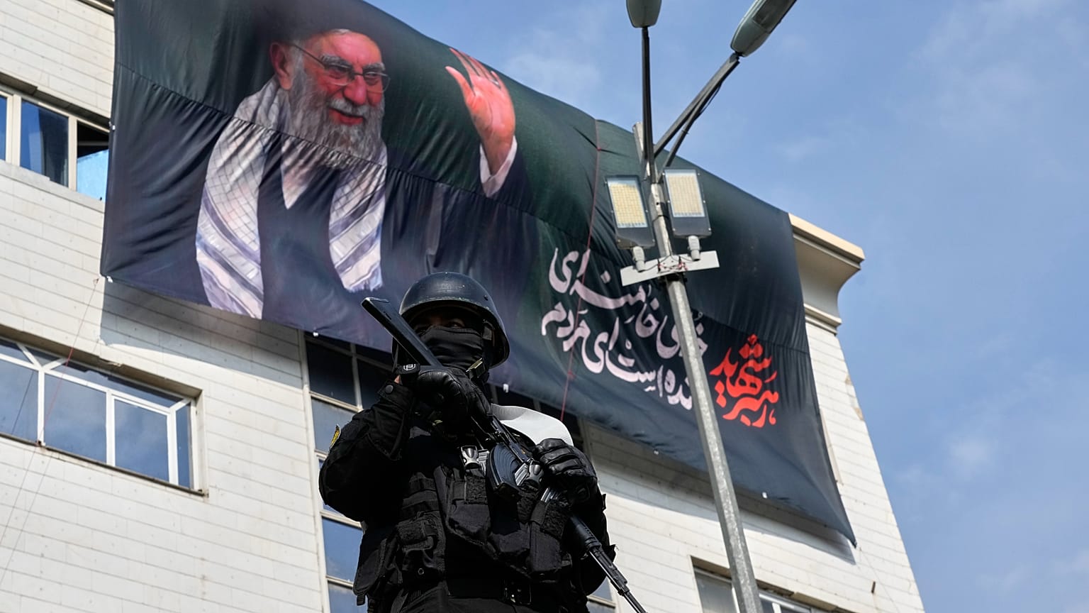 يقف ضابط أمن حارساً خلال مظاهرة لدعم ترشيح آية الله مجتبى خامنئي خلفاً لوالده الراحل، آية الله علي خامنئي، كمرشد أعلى، مع ظهور لوحة إعلانية لعلي خامنئي في الخلفية، في طهران، إ