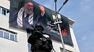يقف ضابط أمن حارساً خلال مظاهرة لدعم ترشيح آية الله مجتبى خامنئي خلفاً لوالده الراحل، آية الله علي خامنئي، كمرشد أعلى، مع ظهور لوحة إعلانية لعلي خامنئي في الخلفية، في طهران، إ