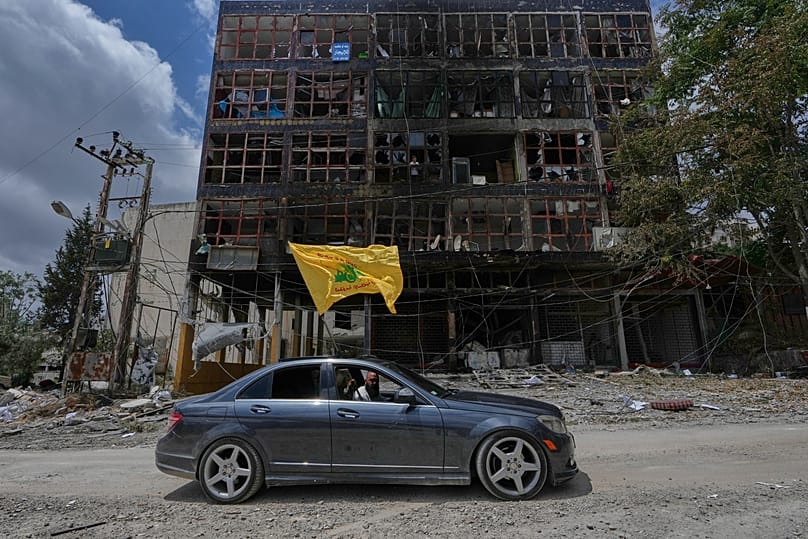 رجل يرفع علم حزب الله أثناء قيادته مركبته أمام مبنى متضرر في مدينة النبطية جنوب لبنان، في 22 يونيو 2026.
