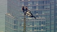 Two people stand on the tip of the antenna of the Empire State Building in New York while holding a banner, 1 July, 2026