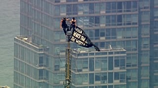 Two people stand on the tip of the antenna of the Empire State Building in New York while holding a banner, 1 July, 2026