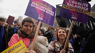 Unas mujeres se manifiestan con carteles “Igual salario ya” y “Solidaridad con las mujeres de todo el mundo”, durante el Día Internacional de la Mujer