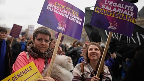Women demonstrate with posters reading "Equal pay now", right, and "Solidarity with women around the world" during a demonstration as part of the International Women's Day, We