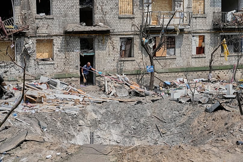A local resident sweeps up the rubble with a missile crater in the foreground in Kyiv, 3 July, 2026