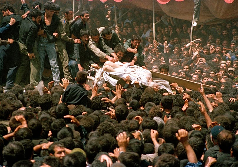 تتدافع حشود من المشيعين للمس جثمان الزعيم الإيراني آية الله روح الله الخميني، بينما يُمرَّر نعشه فوق الرؤوس خلال مراسم الجنازة في طهران، في 6 يونيو 1989