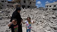 امرأة مع أطفالها تعود إلى قريتهم عقب الإعلان عن اتفاق وقف إطلاق النار الأولي بين الولايات المتحدة وإيران، تمر أمام منزلهم المدمر في قرية دير كانون جنوب لبنان