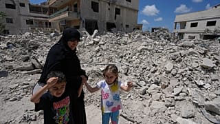 امرأة مع أطفالها تعود إلى قريتهم عقب الإعلان عن اتفاق وقف إطلاق النار الأولي بين الولايات المتحدة وإيران، تمر أمام منزلهم المدمر في قرية دير كانون جنوب لبنان
